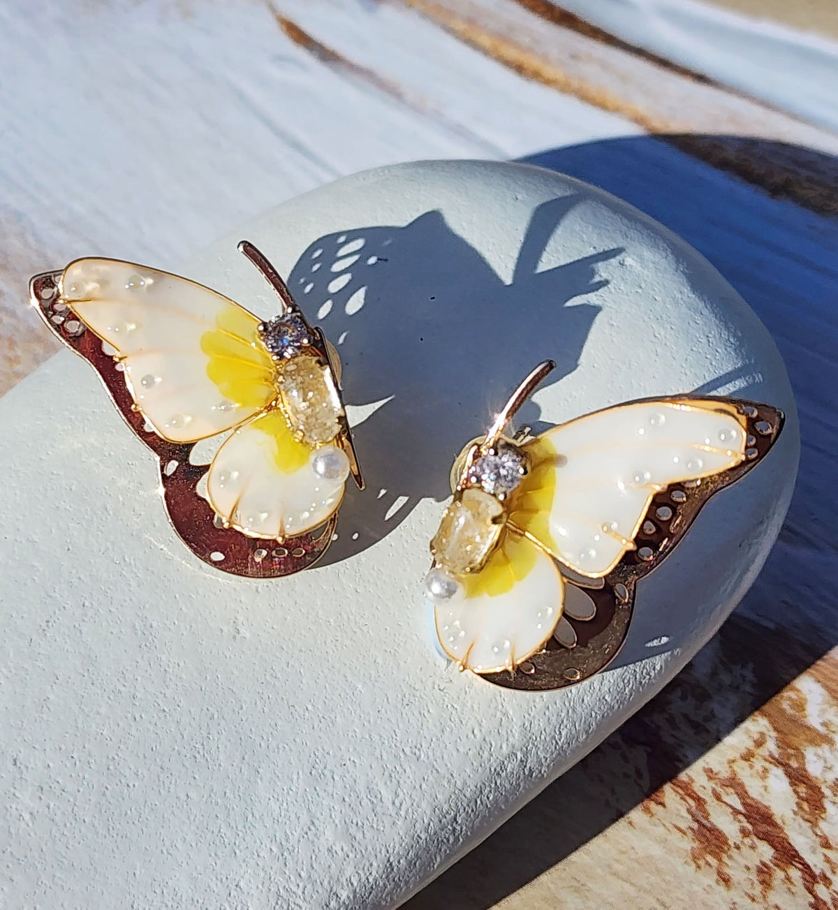 Handpainted butterfly stud earrings with various birthstone-colored resin wings, gold-plated brass, and 12 months' birthstone cubic zirconia center stones, displayed in natural sunlight