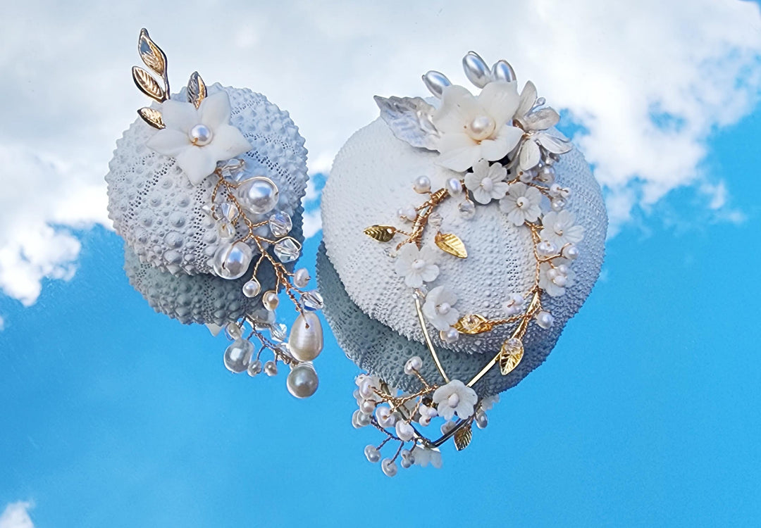 Handmade bridal earrings with freshwater pearls, porcelain flowers, and gold wire details, displayed against a blue sky background