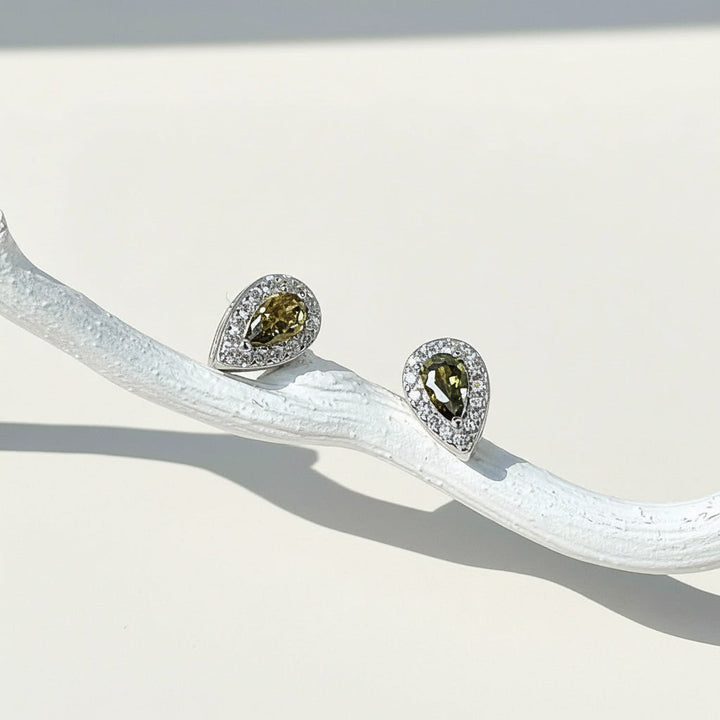 Teardrop stud earrings with olive green birthstone, platinum-plated silver setting, and halo of clear cubic zirconia.