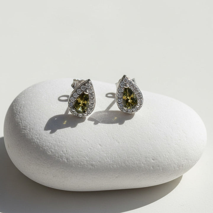 Teardrop silver stud earrings with platinum plating, green birthstone center, and halo of clear cubic zirconia.
