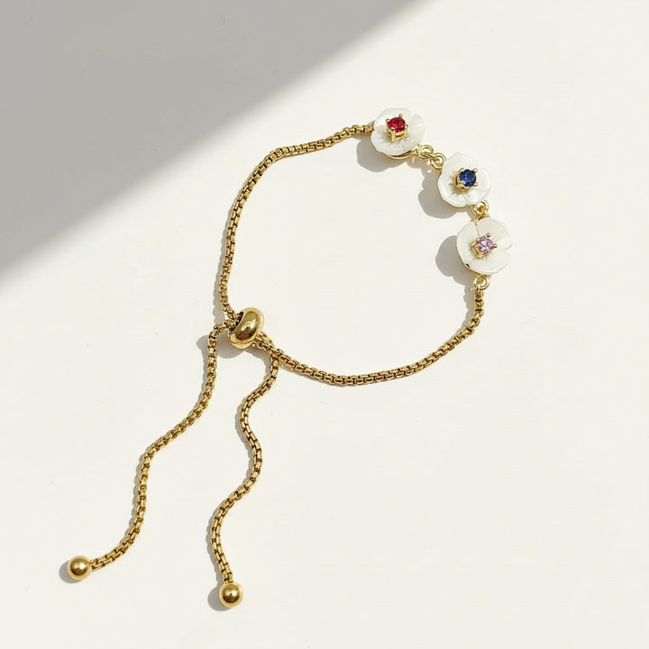 Adjustable gold bracelet with three white mother-of-pearl flowers featuring red, blue, and pink birthstones.