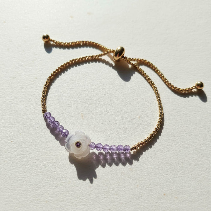 Gold adjustable bracelet with amethyst beads and carved white flower charm featuring a purple gemstone center.