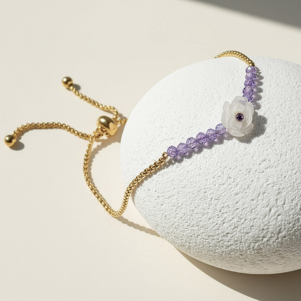 Gold adjustable bracelet with purple beads and white carved flower centerpiece featuring a small amethyst gem