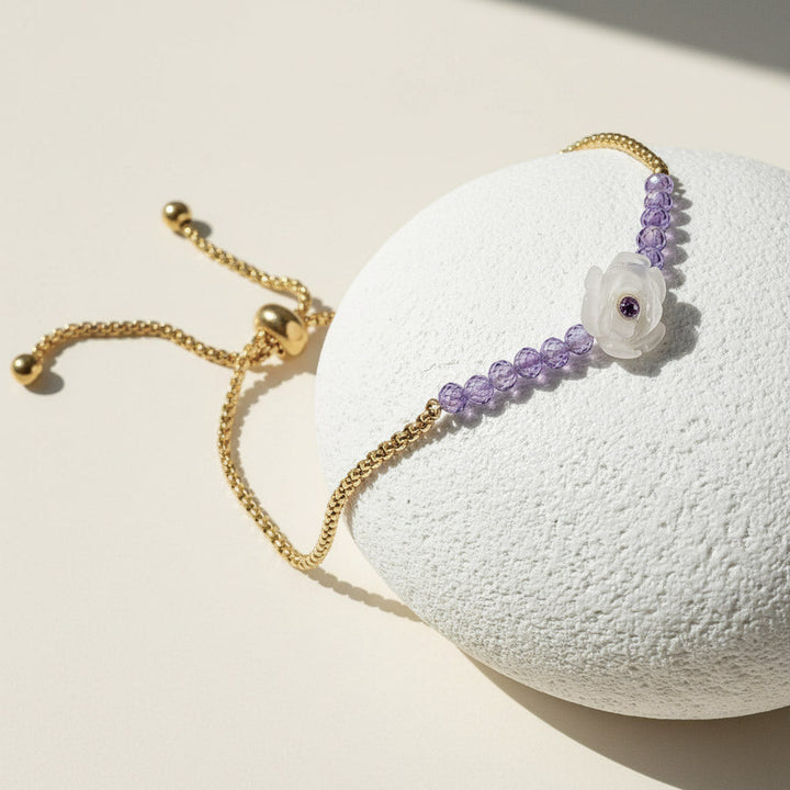 Gold adjustable bracelet with purple beads and white carved flower centerpiece featuring a small amethyst gem