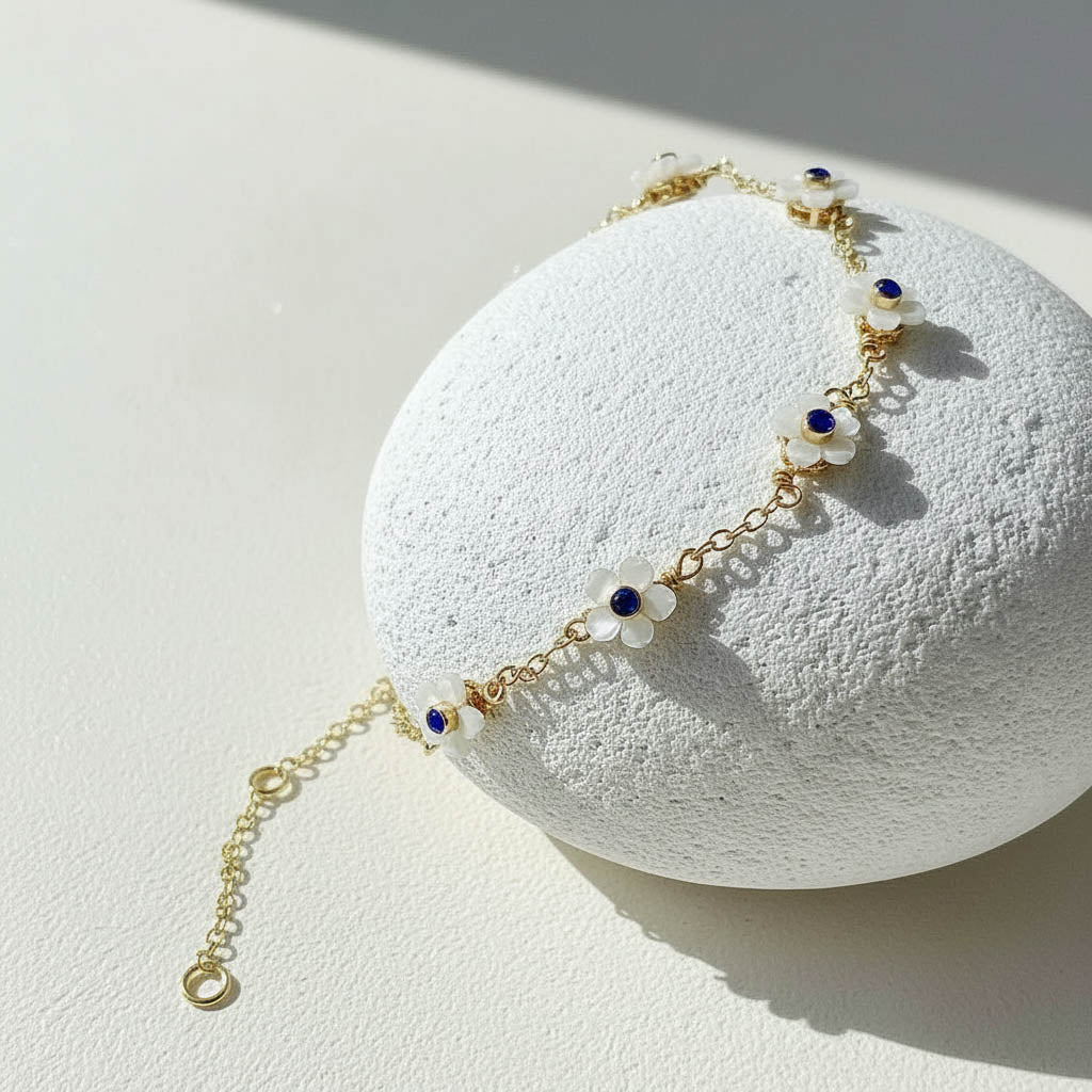 Delicate gold bracelet with blue and white beads on a textured white surface