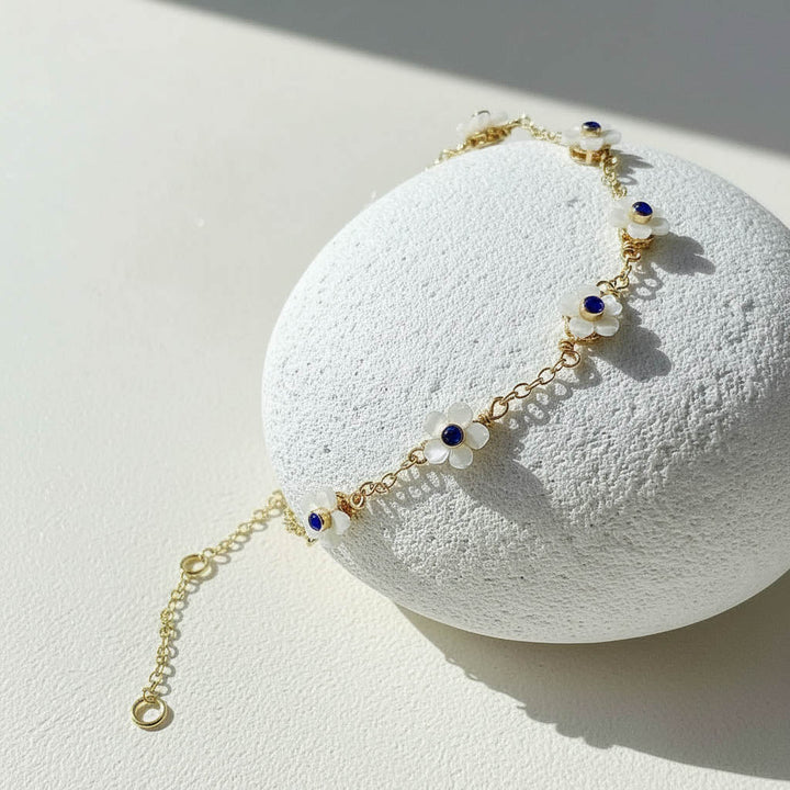 Delicate gold bracelet with blue and white beads on a textured white surface
