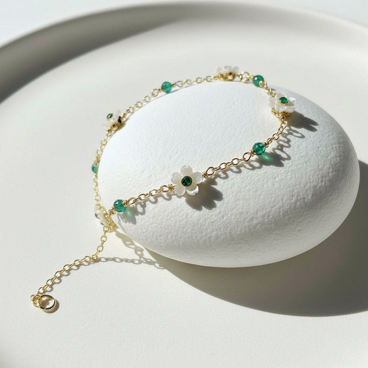 Gold bracelet with green beads on a white stand