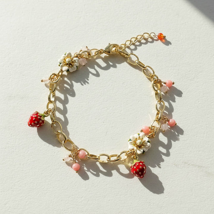 Gold bracelet with strawberry and flower charms on a light background
