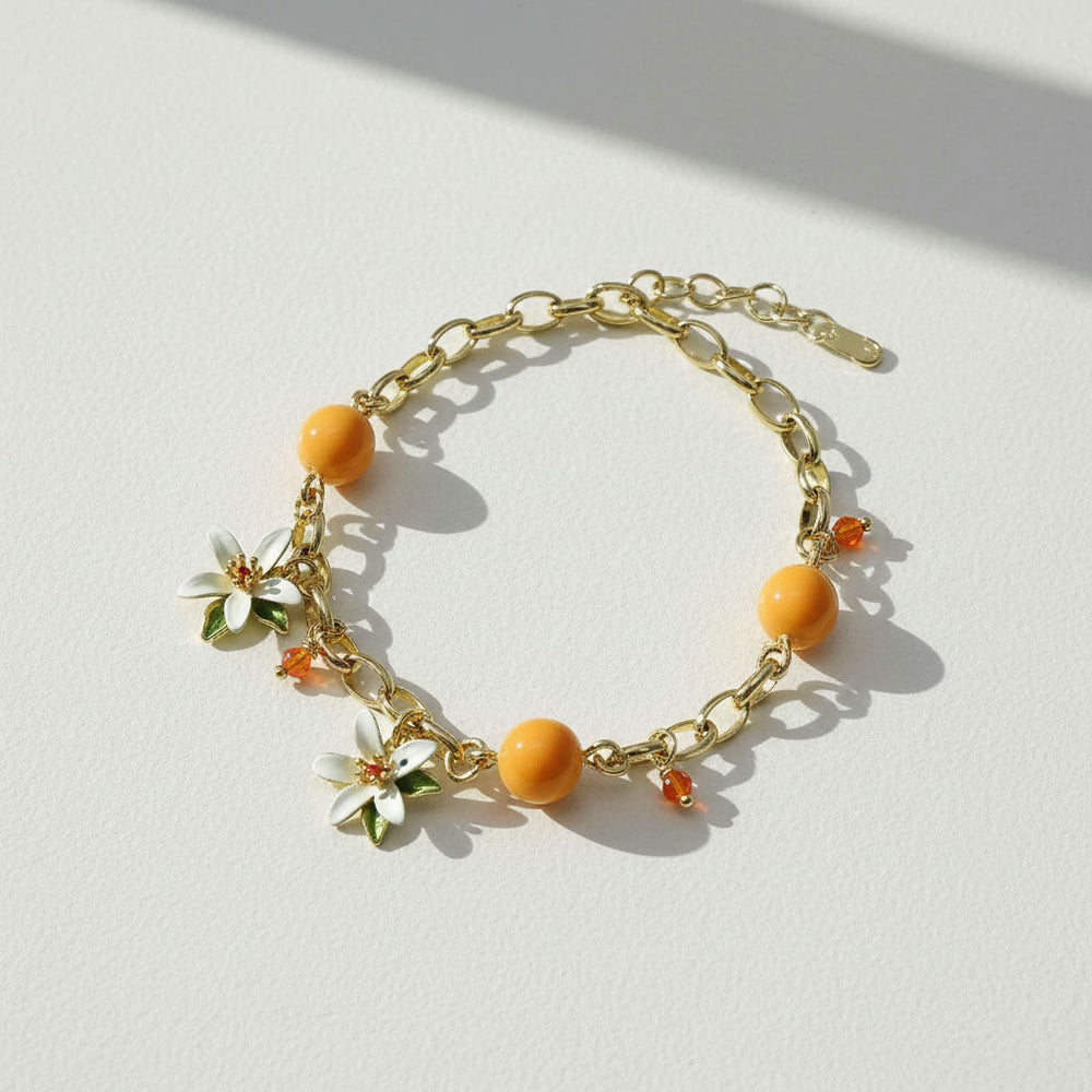 Gold bracelet with orange beads and floral charms on a light background