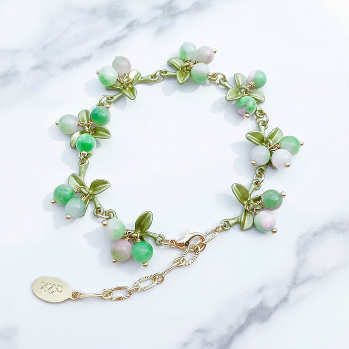 Green beaded bracelet with gold chain on a marble surface