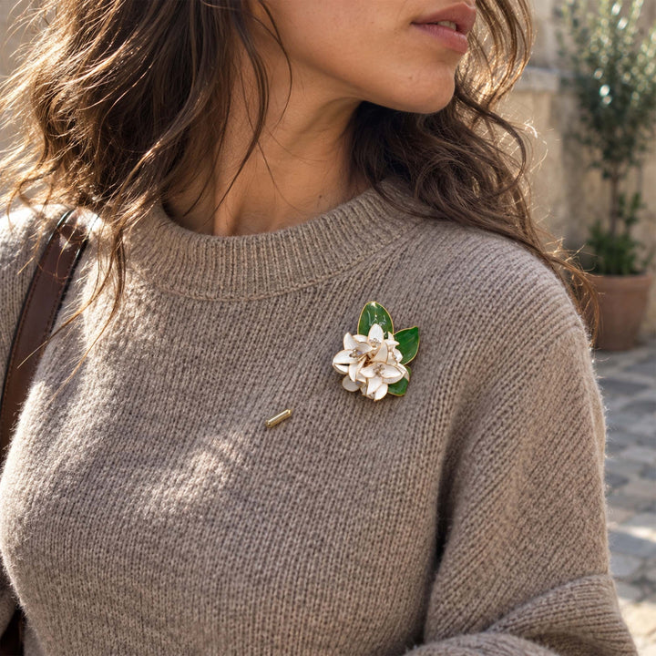A close-up of a woman wearing a taupe knit sweater and a white gardenia floral pin brooch styled on a neutral knit sweater