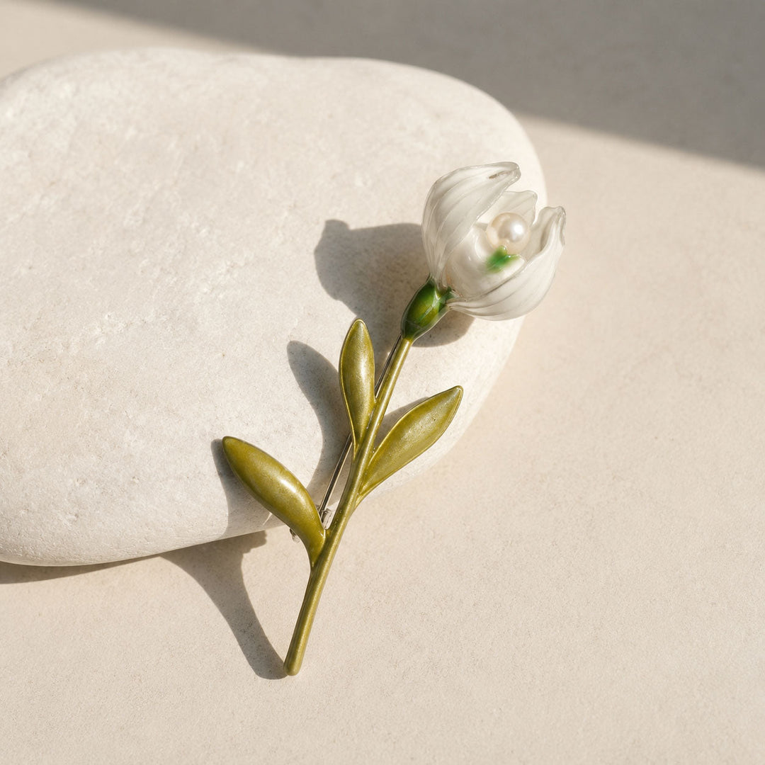 Handcrafted lily of the valley pearl brooch with white enamel bloom and green leaves on a smooth white stone.