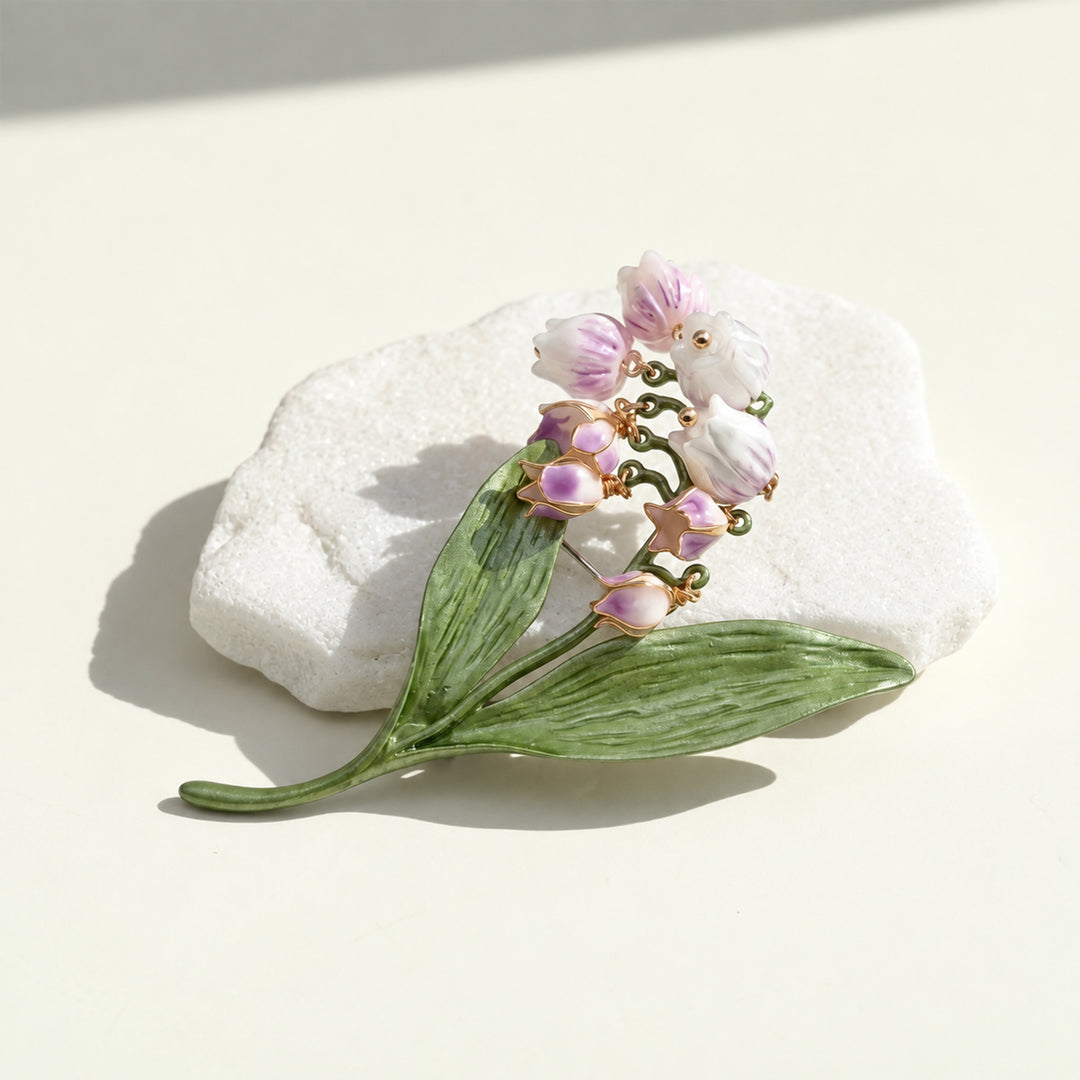 Handcrafted lilac Lily of the Valley floral brooch with white bell-shaped blooms and green leaves on a cream background.