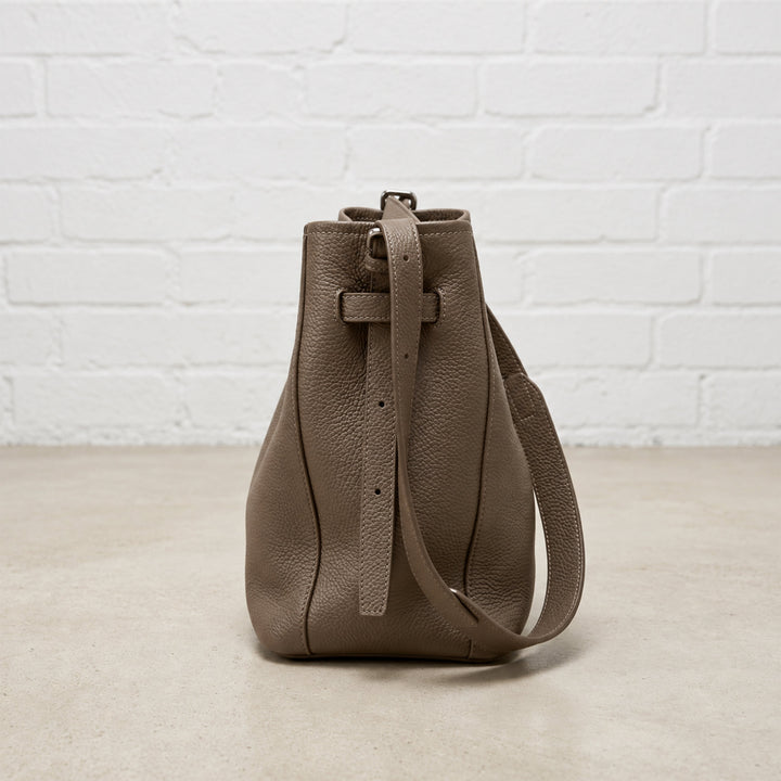 Side view of the Dark Taupe Belted Bucket Bag highlighting its soft structure, leather stitching, and adjustable shoulder strap.
