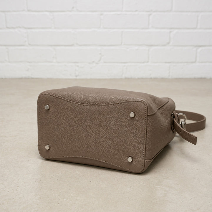 Bottom view of the Taupe Belted Bucket Bag showing its textured leather base, reinforced stitching, and four metal feet.