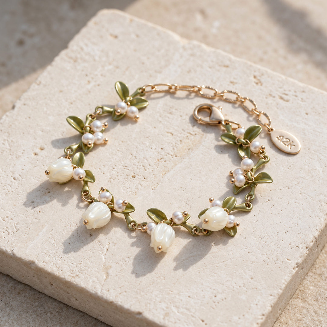 Lily of the Valley pearl bracelet with mother-of-pearl flowers and olive-green enamel leaves on sunlit pale stone.