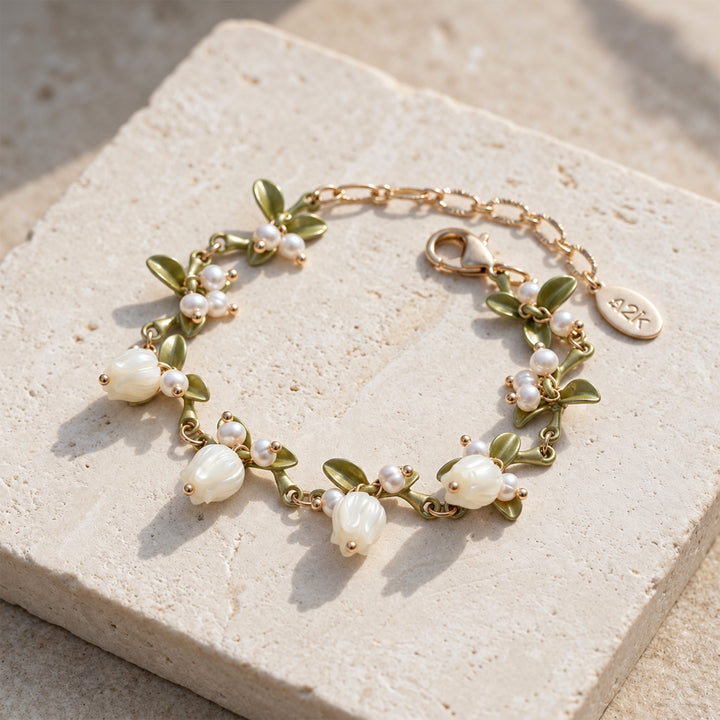 Lily of the Valley pearl bracelet with mother-of-pearl flowers and olive-green enamel leaves on sunlit pale stone.