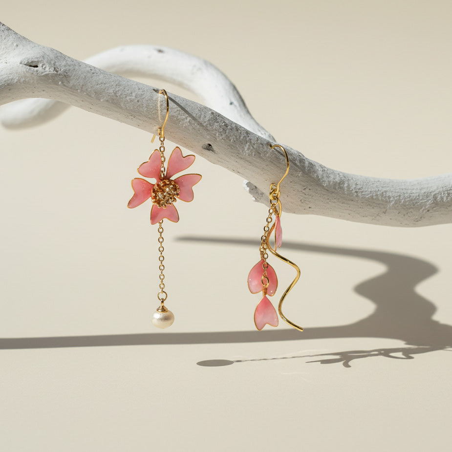 Pink floral earrings with gold chains hanging on a branch against a beige background