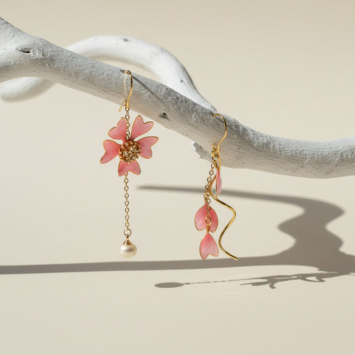 Pink floral earrings with gold chains hanging on a branch against a beige background