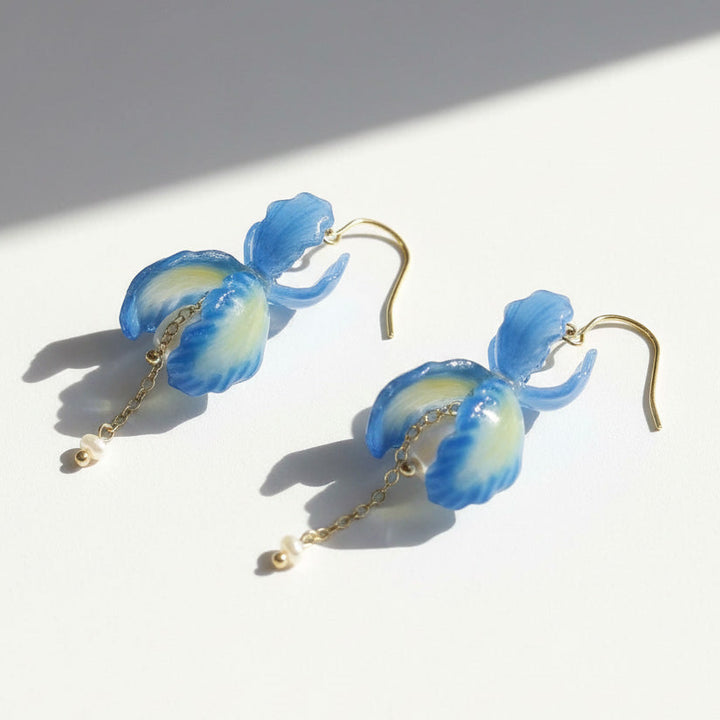 Blue orchid petal drop earrings with pearl and gold chain details, handcrafted floral jewelry on white background.