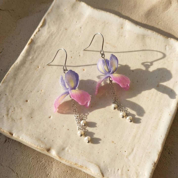 Floral earrings with pink and purple flowers on a ceramic plate.