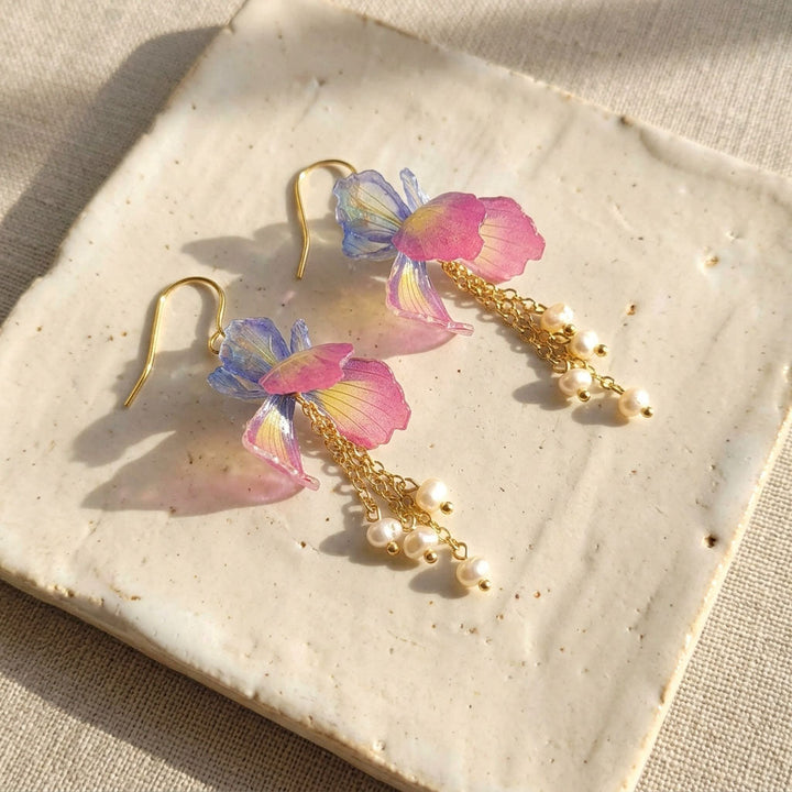 Hand painted Iris earrings with gold chains on a textured surface