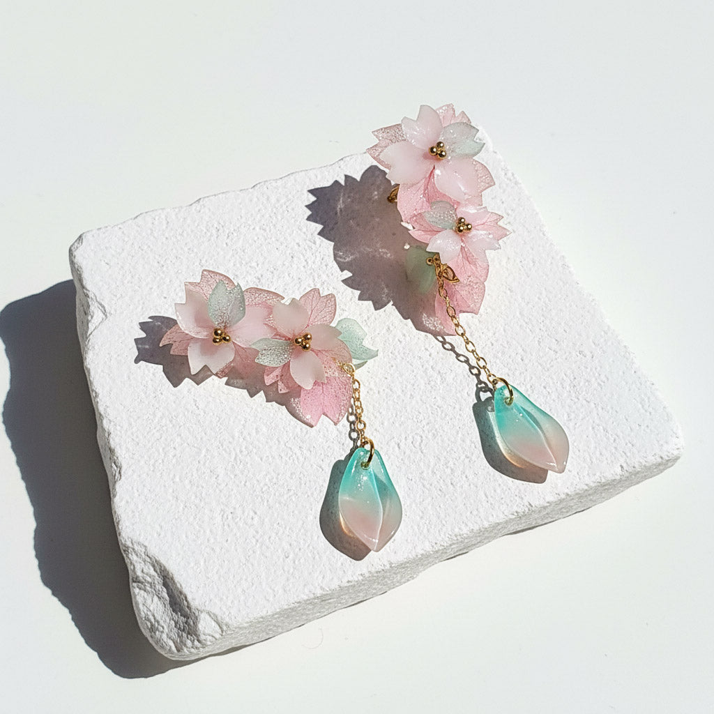 Floral earrings with pink flowers and teal drops on a white stone surface
