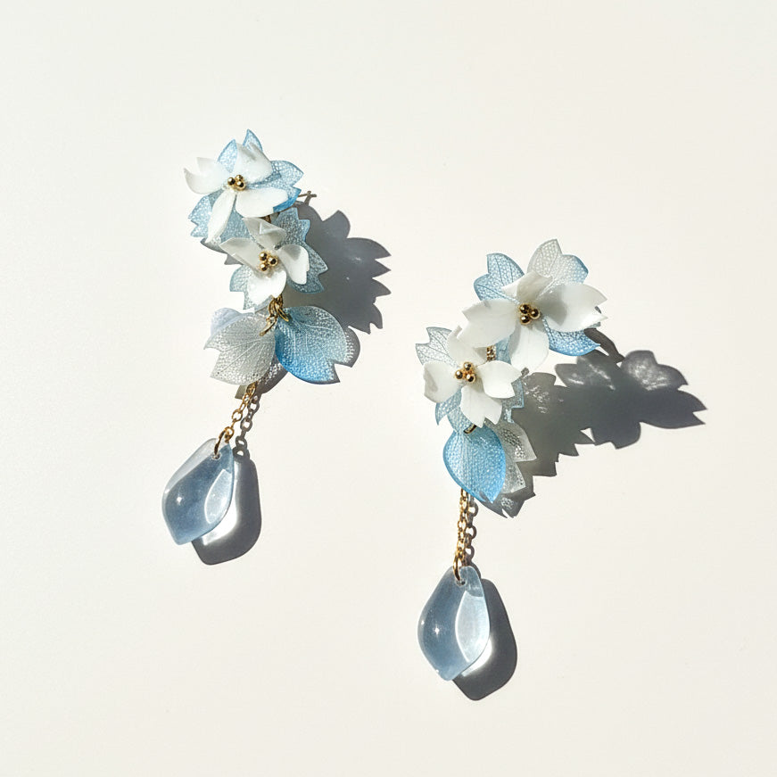 Floral earrings with light blue and white flowers and teardrop-shaped elements on a light background