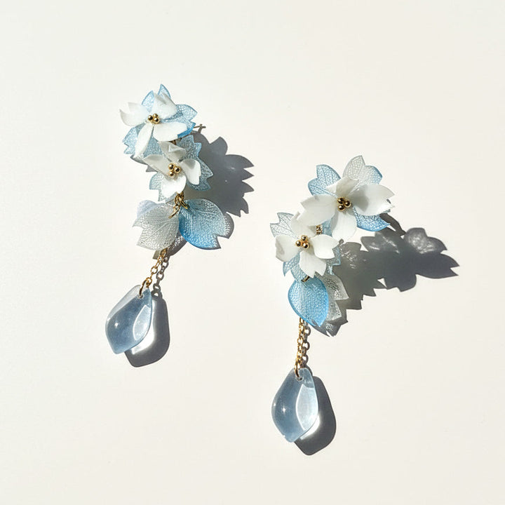 Floral earrings with light blue and white flowers and teardrop-shaped elements on a light background