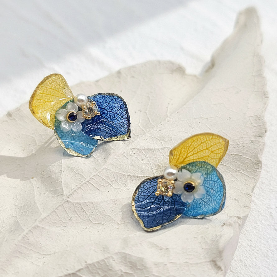 Pair of blue butterfly earrings with gold accents on a white leaf background