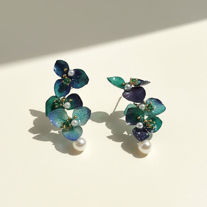 Pair of floral earrings with green and blue leaves on a beige background
