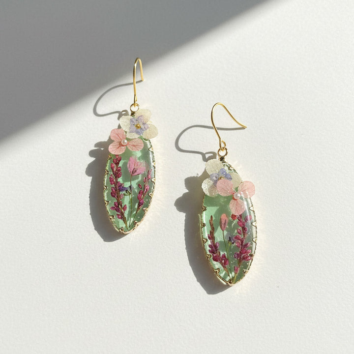 Pressed flower teardrop resin earrings with pink and purple blooms on gold-plated hooks.