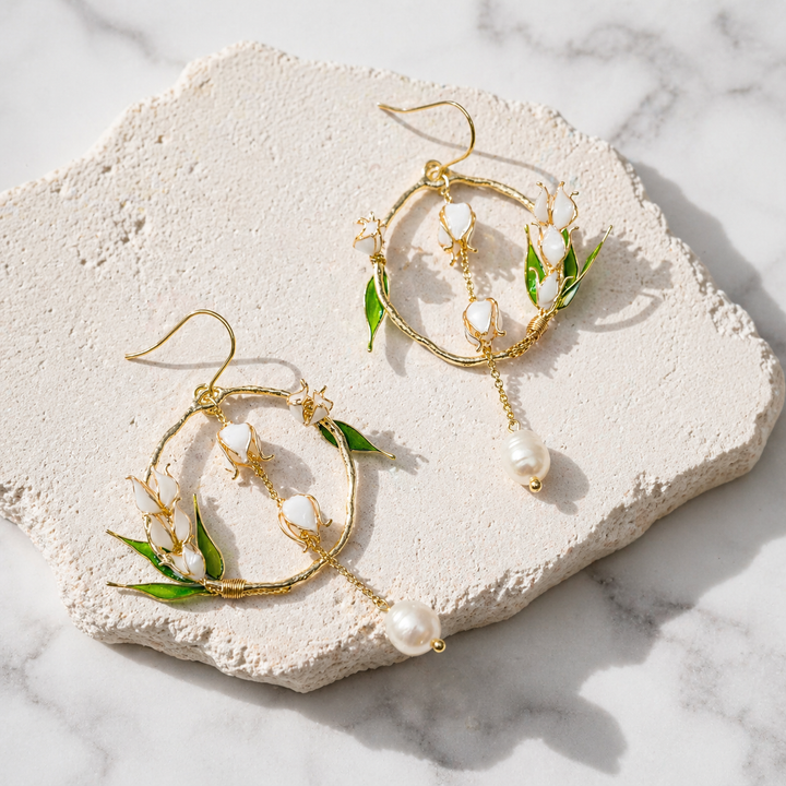 Gold hoop earrings with green leaves and pearls on a textured stone surface.