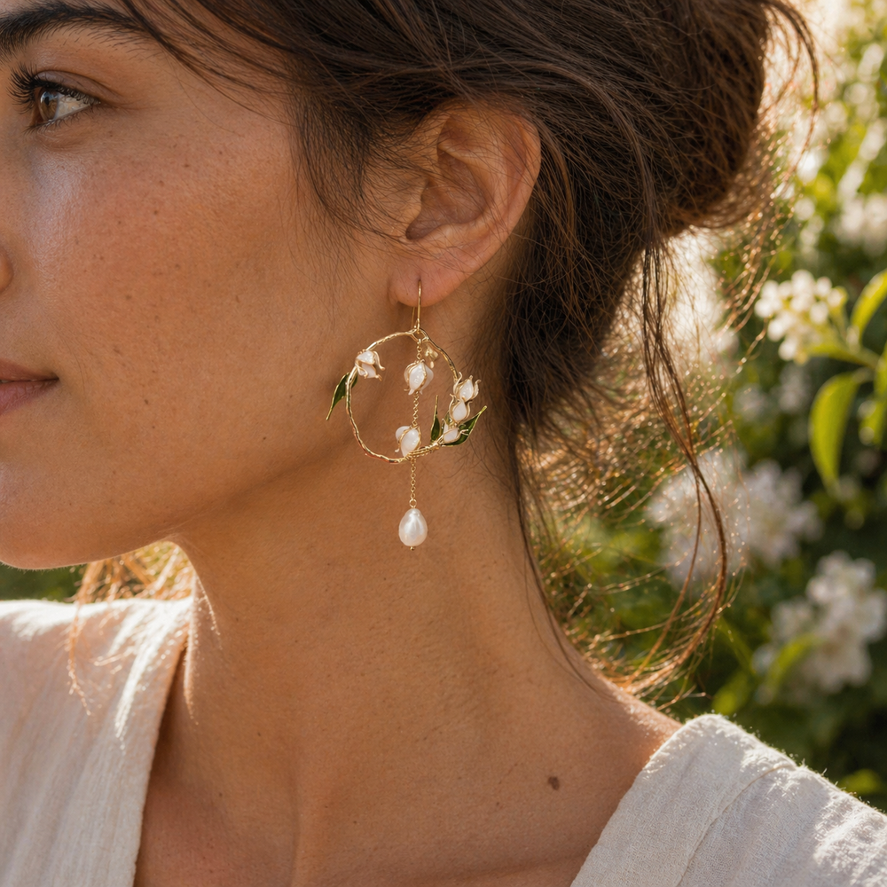 Close-up of a woman wearing gold hoop earrings with freshwater pearl drop and lily of the valley against a blurred natural background.