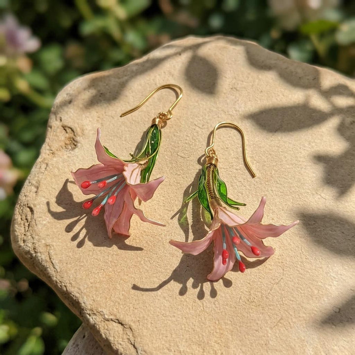 Hand painted lily earrings on a stone surface with a natural background