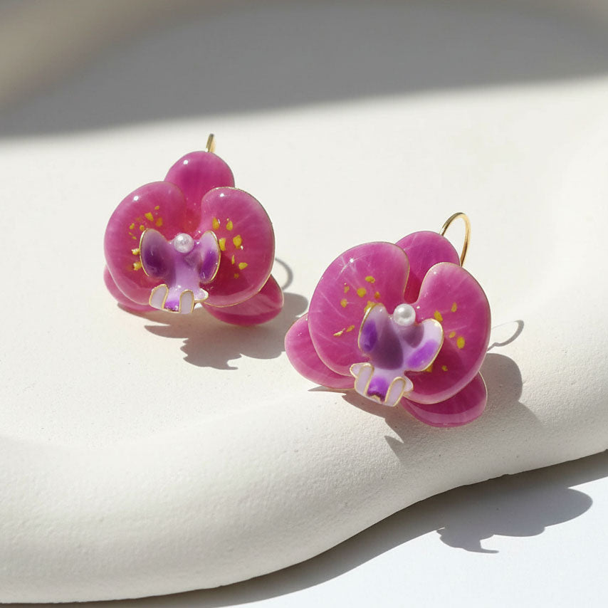 Pink orchid flower earrings with purple centers and pearl accents, handcrafted resin floral jewelry on soft beige background.