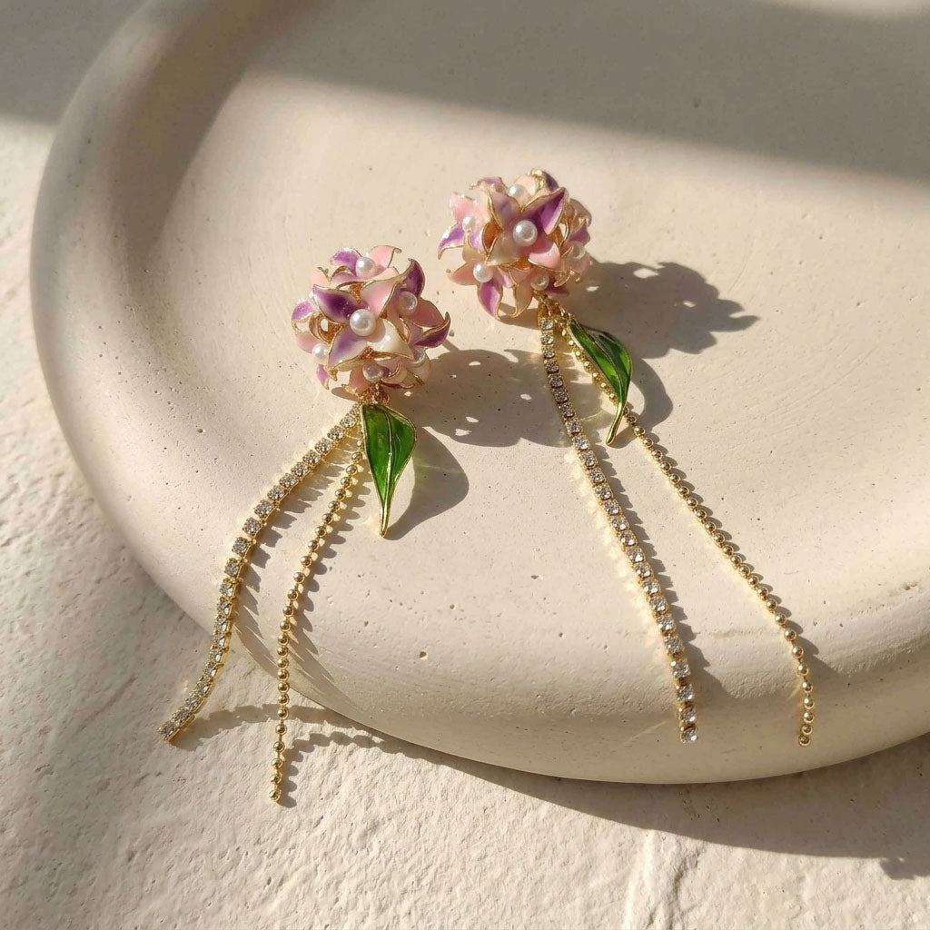 Pair of Hydrangea earrings with gold chains on a light stone surface