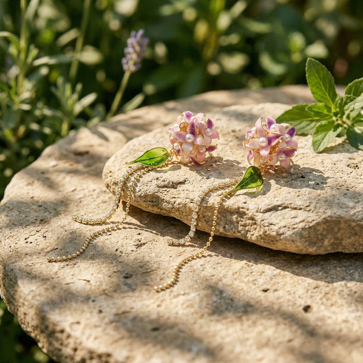 Pair of pink Hydrangea earrings on a stone surface with greenery in the background