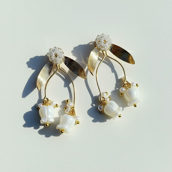 Gold and pearl earrings on a light gray background