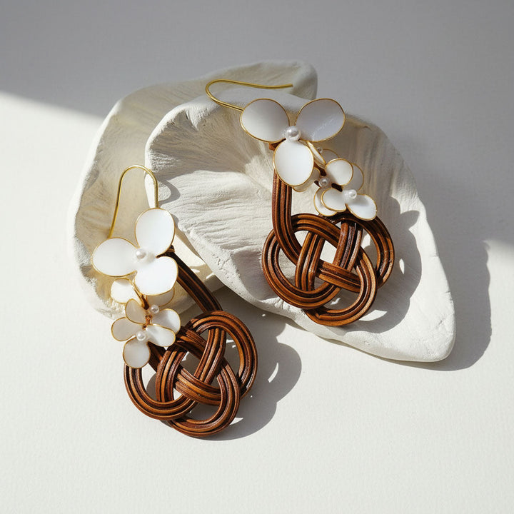 Pair of earrings with woven design and white floral elements on a light background