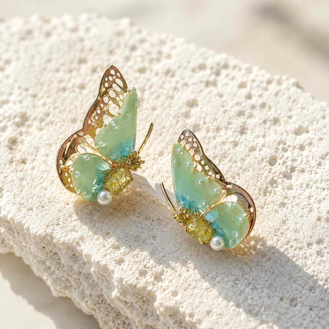 August birthstone butterfly-shaped earrings with gold and green details on a textured white surface