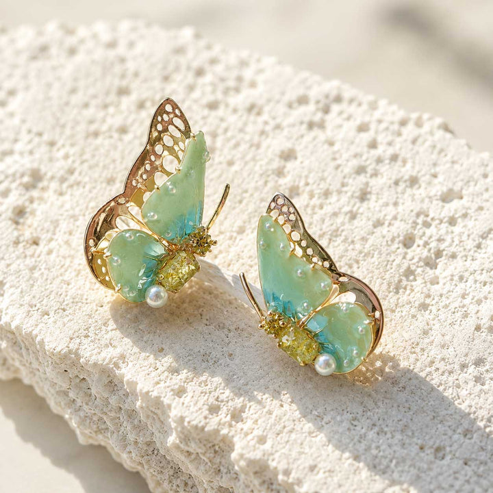 August birthstone butterfly-shaped earrings with gold and green details on a textured white surface