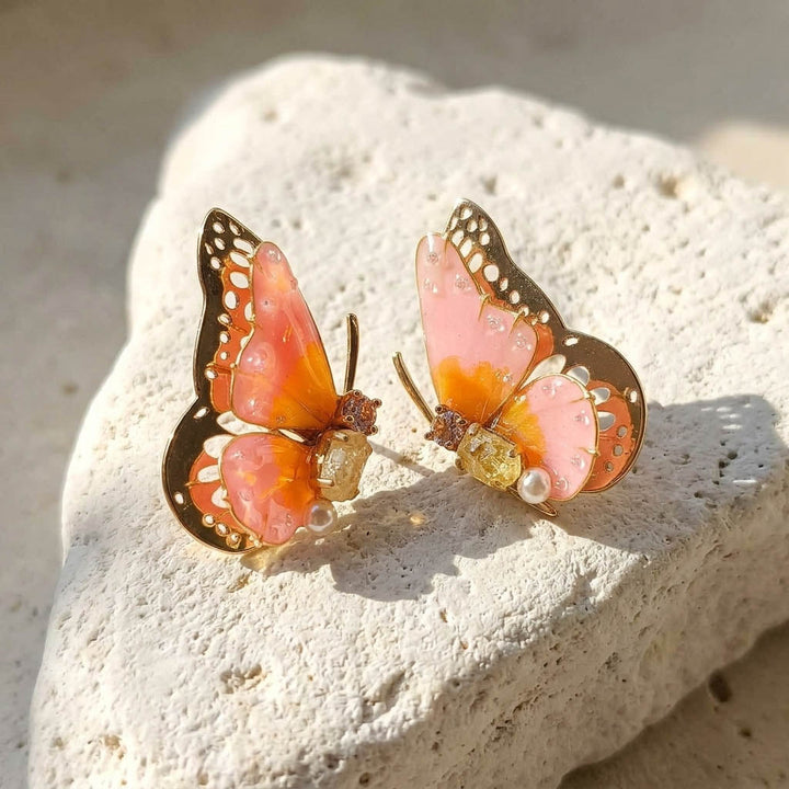 October birthstone butterfly-shaped earrings with pink and orange colors on a stone surface