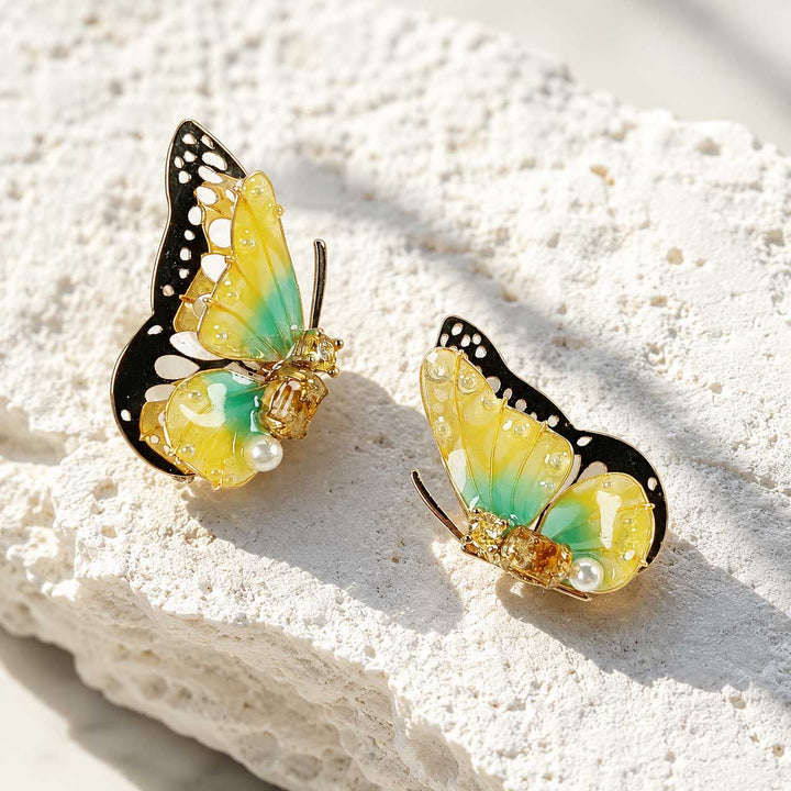 November birthstone butterfly-shaped earrings with yellow and green wings on a textured white surface