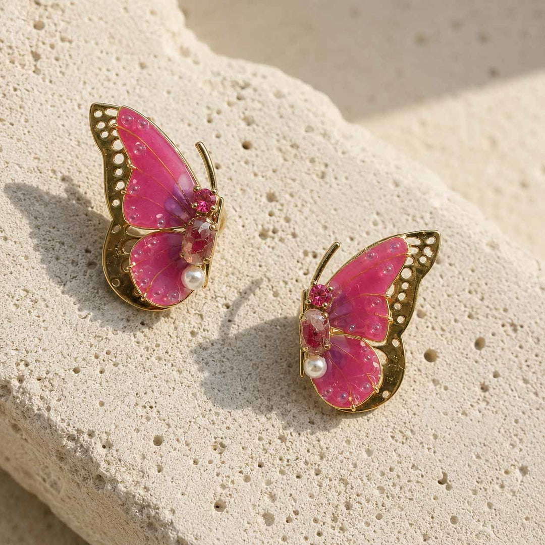 July birthstone Butterfly-shaped earrings with pink wings and gold frames on a textured stone surface.