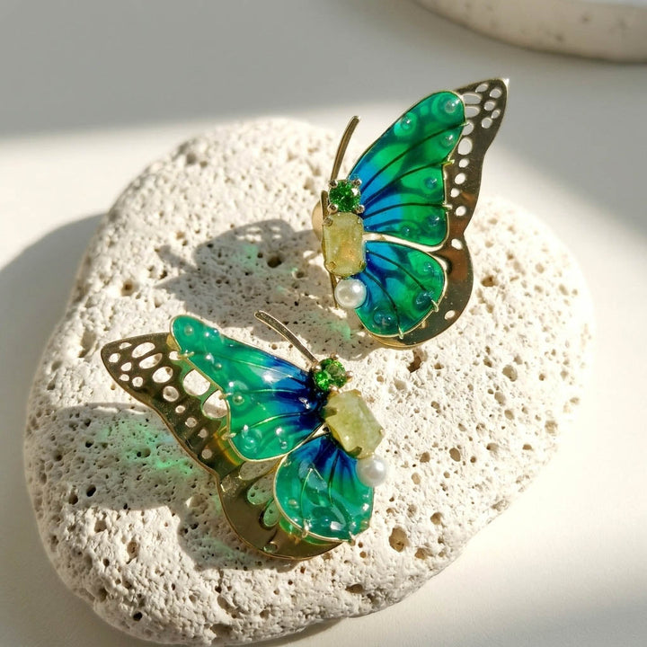 May birthstone butterfly earrings on a textured stone surface