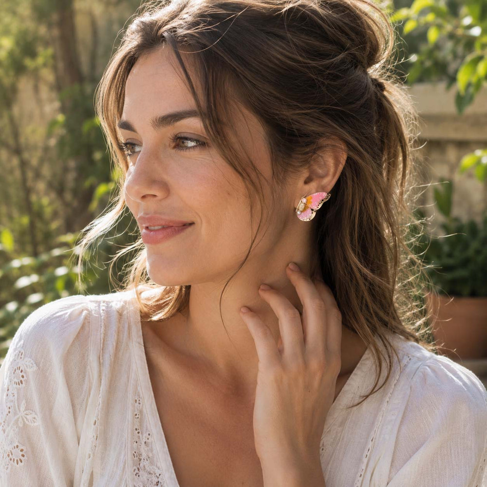 Woman wearing butterfly birthstone earrings outdoors with greenery in the background