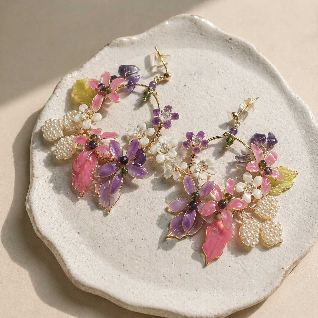 Floral earrings with pink, purple, and white flowers on a textured stone surface.