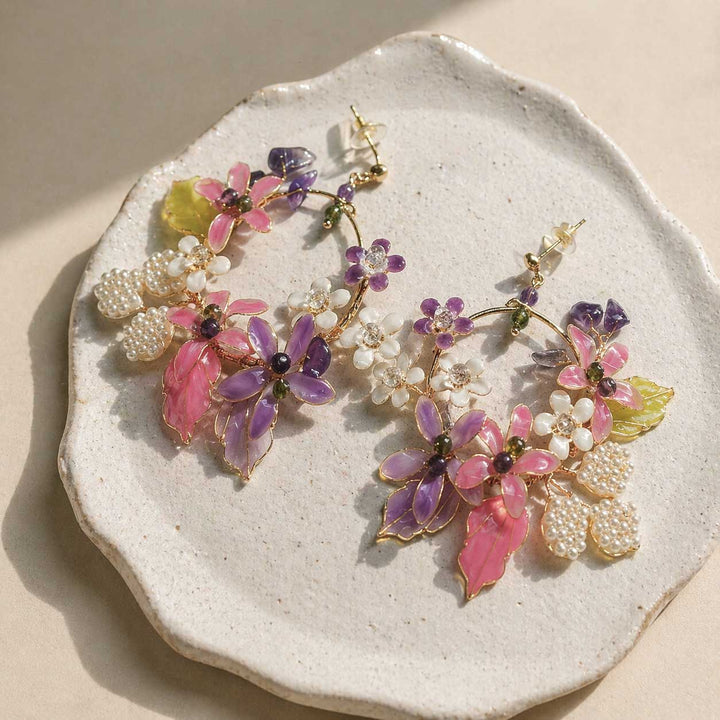 Floral earrings with pink, purple, and white flowers on a textured stone surface.