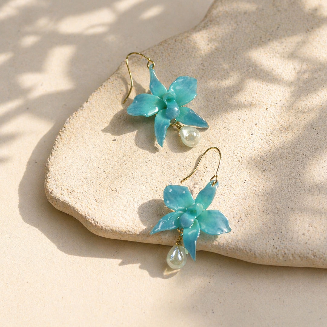 Pair of turquoise orchid-shaped earrings with pearl drops on a beige stone surface.